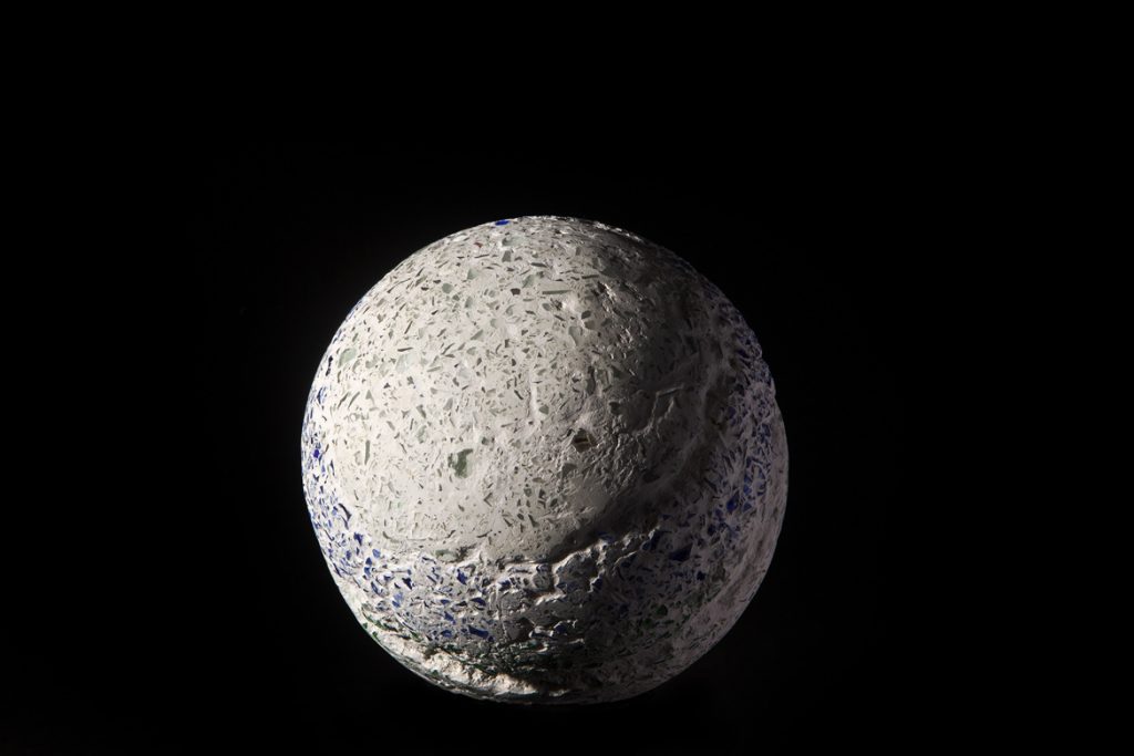 A sphere made of imploded blue and green glass and concrete by Rebecca Newnham, photographed against a black background. Photographed by David Bird.