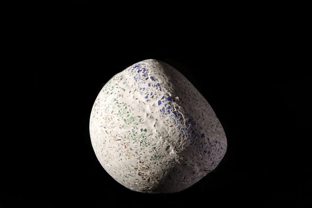 A misshapen sphere made of imploded blue glass and concrete by Rebecca Newnham, photographed against a black background. Photographed by David Bird.