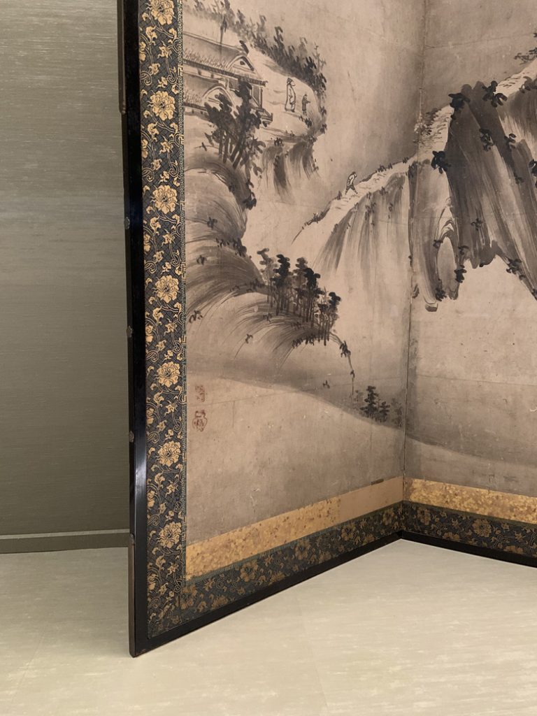 A photograph of a screen in the Tokyo National Museum in Japan. It shows a man walking along a mountain ridge. Photographed by Rebecca Newnham.